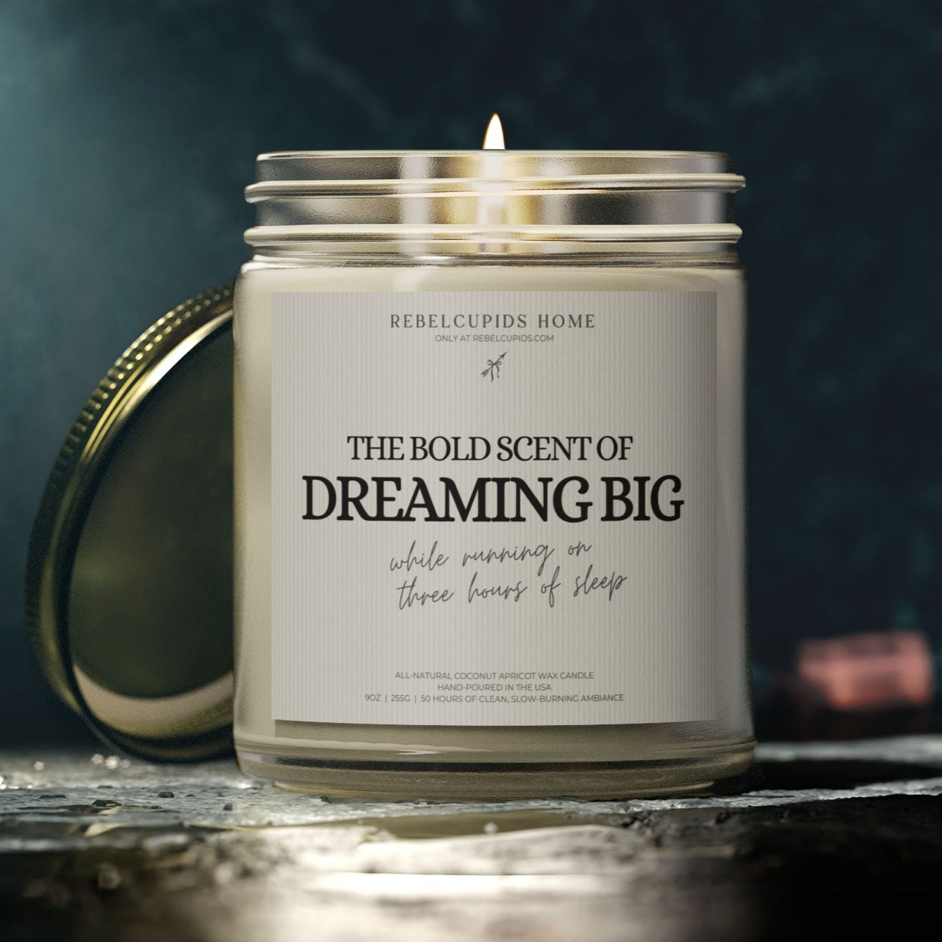 Candle with a label reading 'The Bold Scent of Dreaming Big' on a dark background