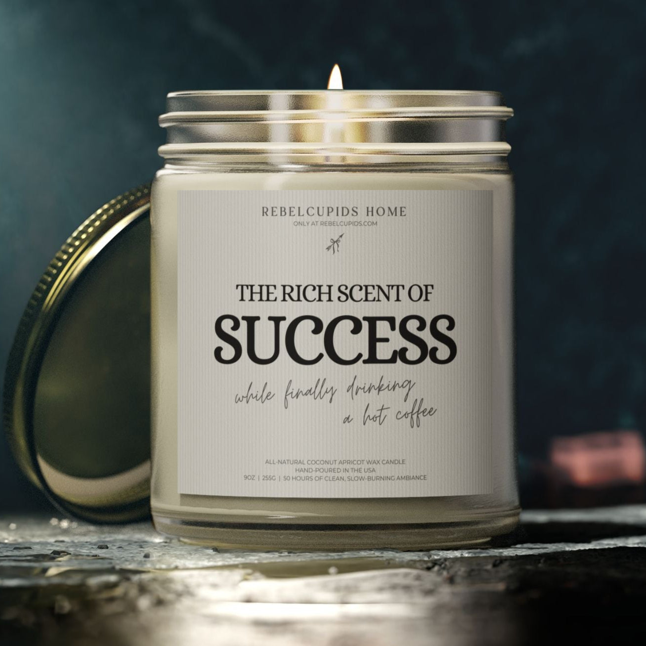 Candle with a label reading 'The Rich Scent of Success' on a dark background